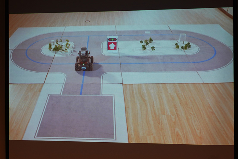 AIを使用した自動運転が行われている様子。ロボットが青のライン上で動作し、途中に信号機のマーカーを置くことで発進や停止の制御が行われている。