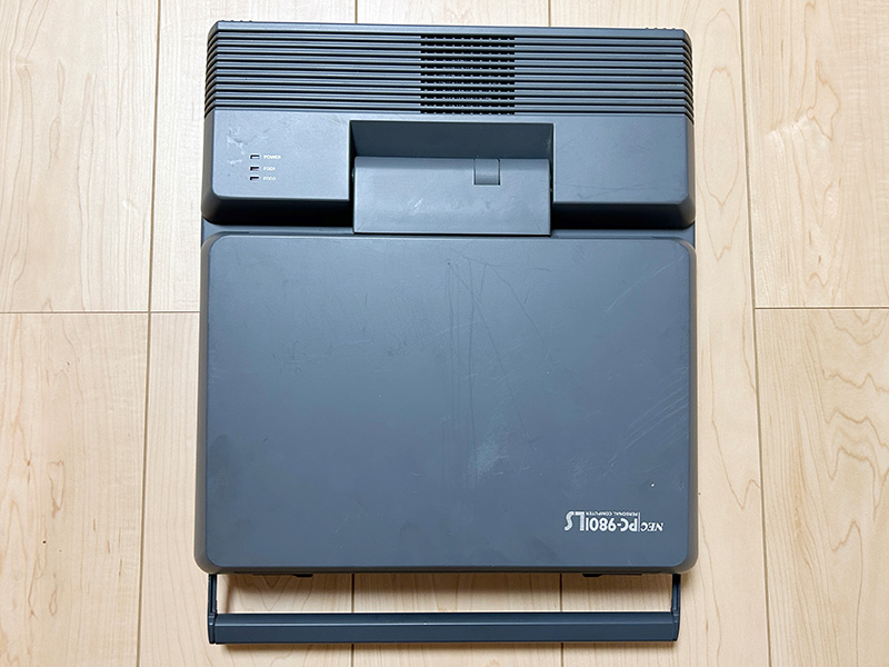 キーボード部分を真上から見た状態です。かなりコンパクトになっているものの、基本的なキーに関しては問題無くタイピングすることができました。キーボード右上部分には、メモリを増設するためのスロットが用意されています。蓋を閉めると左側に電源とFDDのインジケータが見えますが、これは稼働中にも見えるようになっていて、FDDへアクセスしていることは右側面のFDDを見なくてもわかるようになっていました。手前に引き出されているのが取っ手で、かなりしっかりしています。