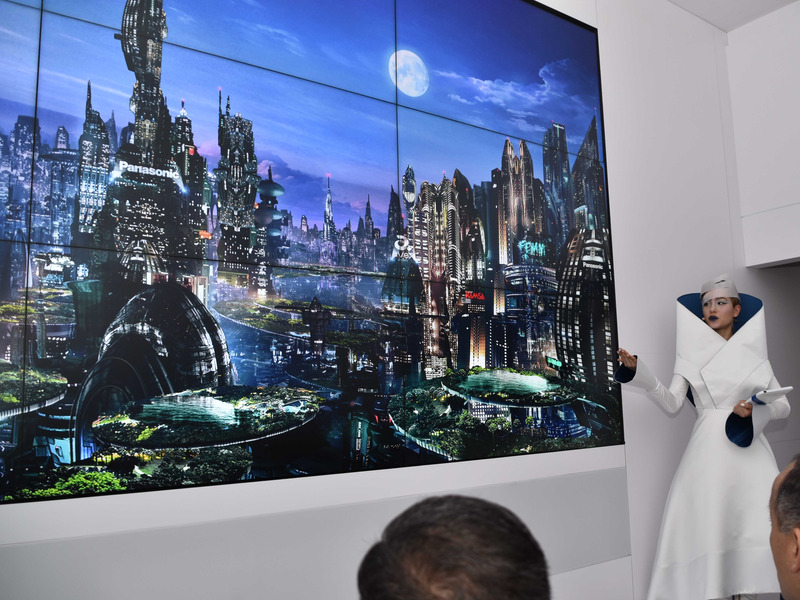 部屋の右からソフィー登場。メインの衣服は春巻き風。頭の頭巾は生春巻き風だ。前と左右に映し出されている映像は未来都市の様子。このあとソフィーに連れられ別室へと移動