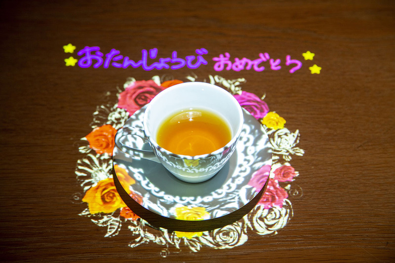 テーブル上の飲み物が入ったカップを飾る映像を投写
