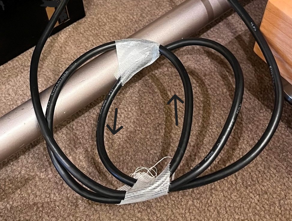 写真3：電源ケーブルの半径ずらし。矢印は電流の向きを示し、中央で互いに逆方向になることを示す。これで同相(コモンモード)の成分を抑える力が弱くなる
