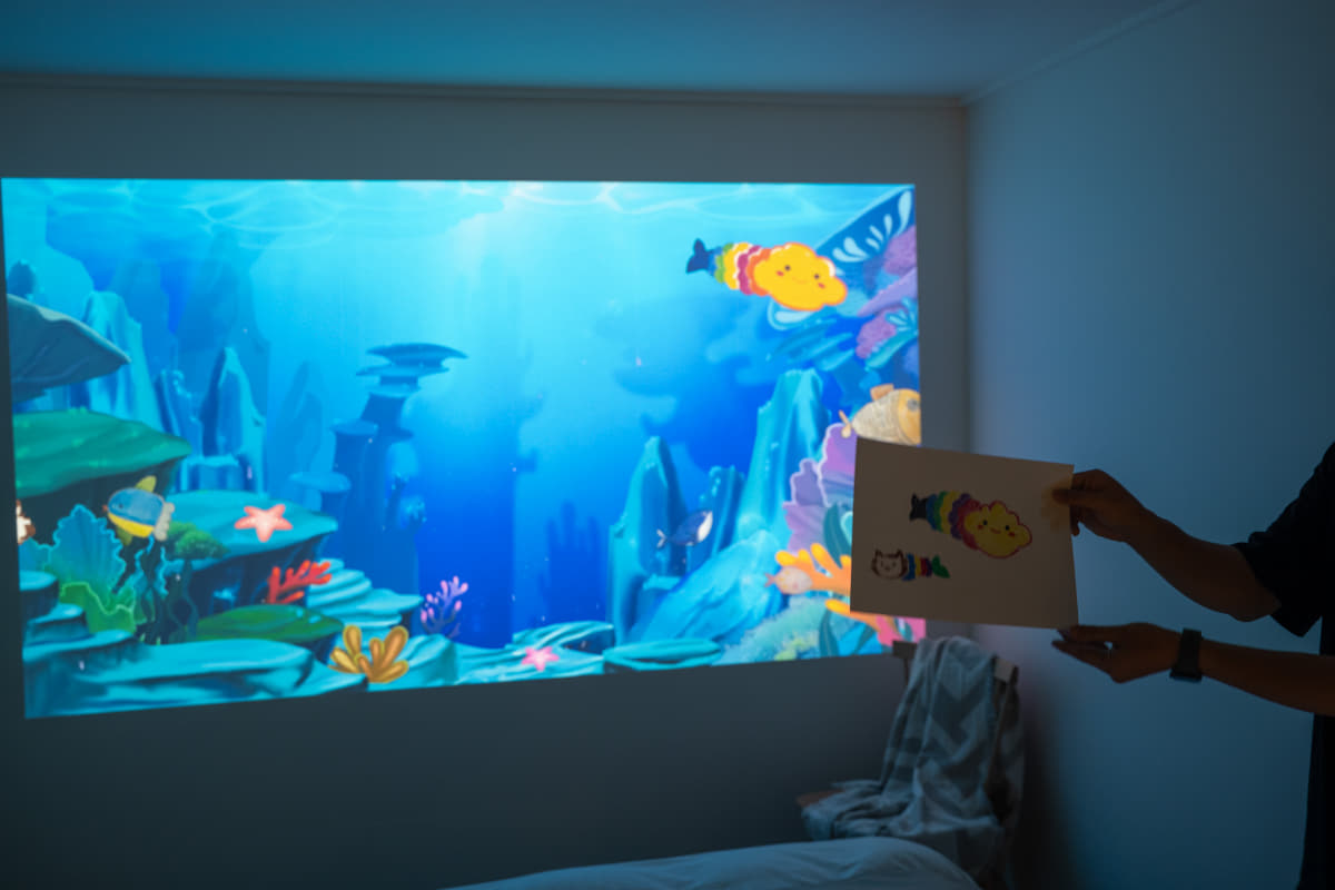 描いた魚の絵を取り込み、投写した海の中で泳がせるアプリ