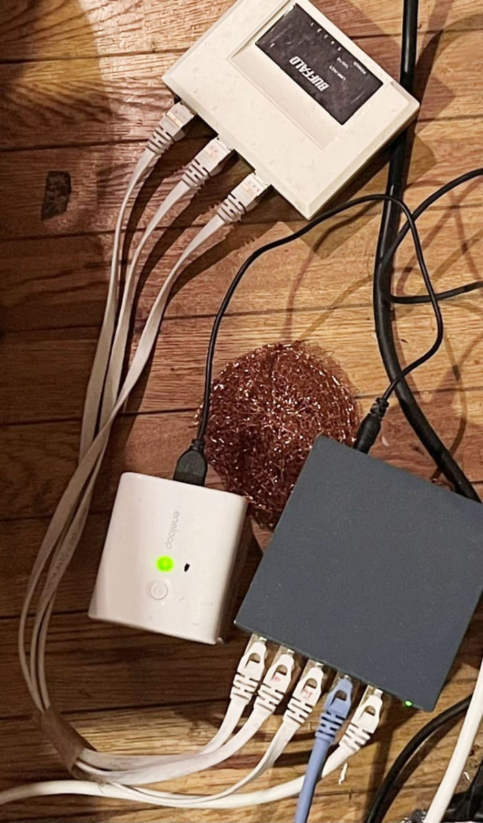右下の灰色の箱がスイッチングハブ。右端のLANケーブルはネットワークプレーヤーへ。その隣の青いLANケーブルはルーターからの接続。これをデータの入力とみなしてLANケーブルの交差では、右端のLANケーブルより上に配線している。残りの3ポートは上の通電していないスイッチングハブに接続してノイズ対策している。受け側は端子を一つずつ空けていることに注目。この方が画質、音質がいい。スイッチングハブの隣の緑に点灯しているのはDC5Vの充電池パック。付属のACアダプターよりクリーンな画質、音質になる。商用電源ライン(AC100V)から隔離されるので大きなノイズのループを削除したことになる。ただし、画質は良好だが、「電池臭い」音という癖もないではない