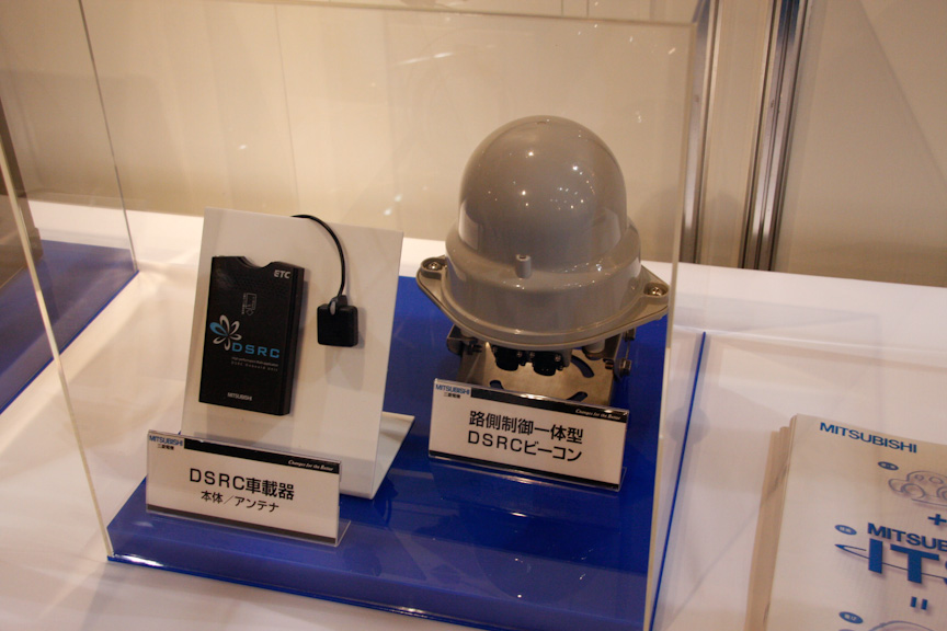 三菱電機はDSRC車載器とリンク可能なカーナビを展示。また、左の写真の丸いものは路側DSRCビーコンで、通常別体となる制御機とアンテナ部を一体にし、小型化している