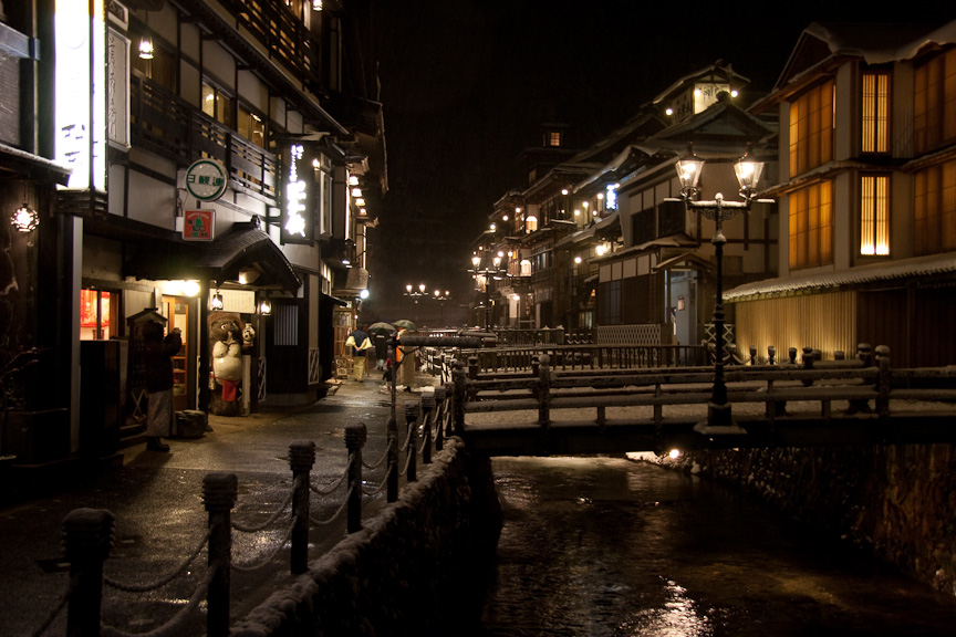 夜の銀山温泉。銀山温泉では再び雪に。旅館にともる明かりが川に映し出され、箱庭的風景が広がる