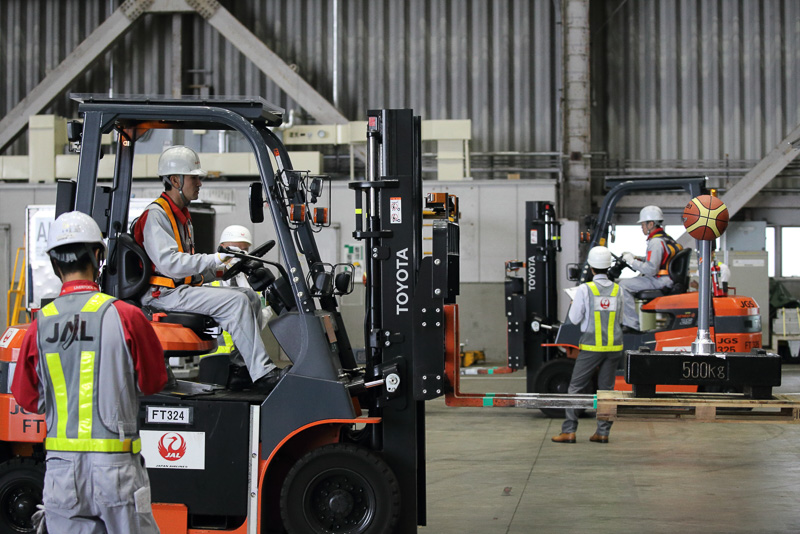 乗車前に目視による各部の点検を行ない、2つのコンテナの荷物の入れ替え作業を行なう出場者。ポールの上のボールを落とせばその時点で即失格だ