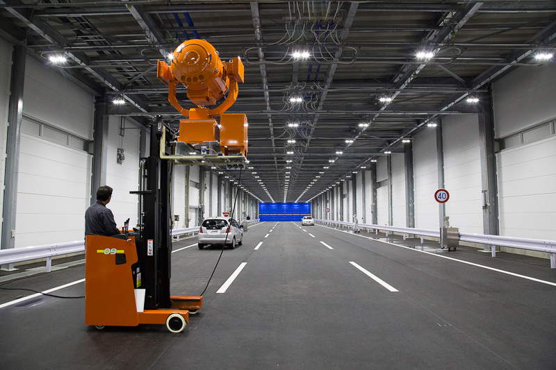 巨大な投光器を使う日照設備。本来は建物の奥側から入り口（メディアの見学位置）に向けてセットしているが、光を直接見るのは危険とのことで反対向きで日照設備のデモが行なわれた。逆光時に前方だけでなく、路面の白線が読めるかのテストも行なわれる