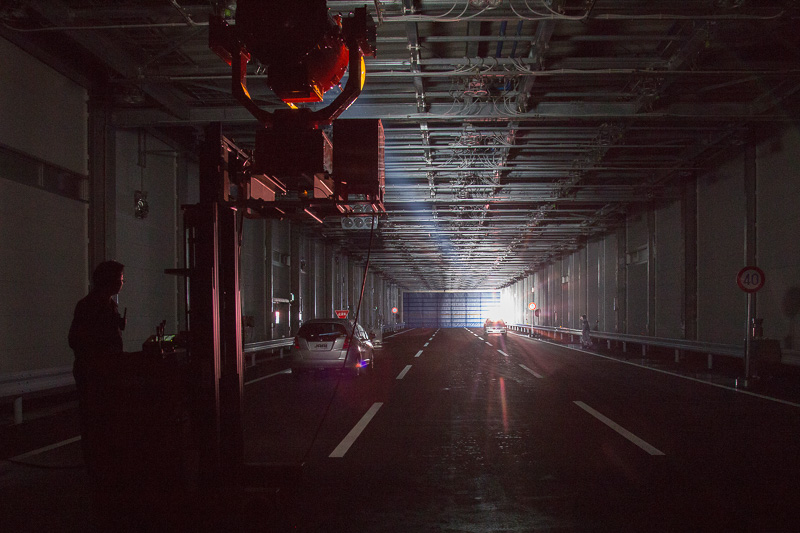 巨大な投光器を使う日照設備。本来は建物の奥側から入り口（メディアの見学位置）に向けてセットしているが、光を直接見るのは危険とのことで反対向きで日照設備のデモが行なわれた。逆光時に前方だけでなく、路面の白線が読めるかのテストも行なわれる