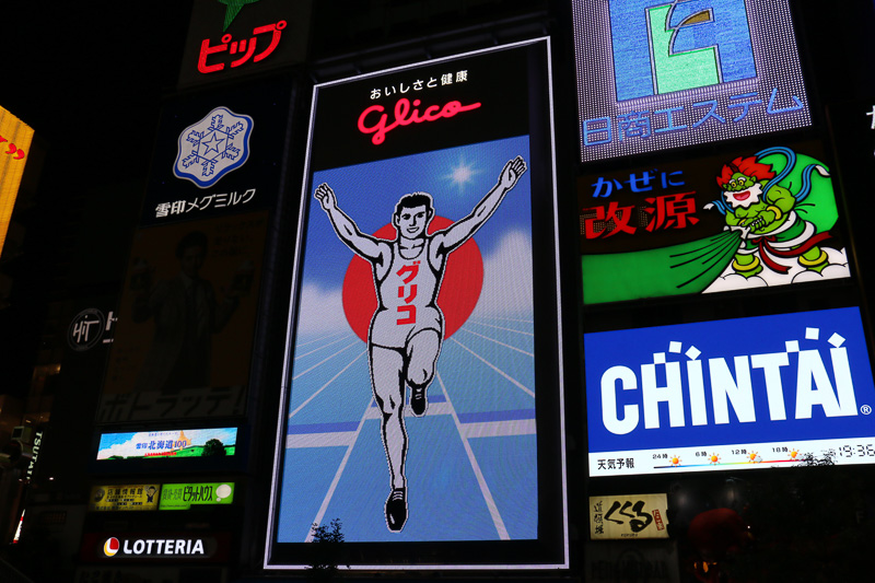 日没後に点灯したあとも、グリコサインはしばらく通常の演出を実施。2014年から6代目にリニューアルした現在のグリコサインは14万個のLEDを照明に使っており、ゴールを駆け抜けていたり、時間帯が朝から夜に移り変わるといったアニメーションを披露している