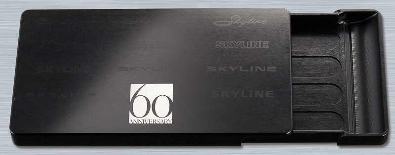 「ジュラルミンカードケース」は航空・宇宙産業で採用されている「A2017」と呼ばれるジュラルミン無垢材を使用。直径3mmの極小ベアリングを4個内蔵することで滑らかな開閉を可能として、本体内部に採用したスプリングと銅球を使用したラッチ機構により心地よい開閉感を得ることができる。写真は「スカイライン60周年記念モデル」（1万2000円）