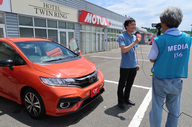 レースの模様を生中継している「<a href="http://ch.nicovideo.jp/carwatch">Car Watch ニコニコチャンネル</a>」と「<a href="https://www.youtube.com/watch?v=S14i9dbctas">YouTube Car Watch Channel</a>」では、レース以外にも谷川編集長（右）が“突撃レポーター”としてサーキットの各所に足を運び現地の模様を定期的に紹介中。新型フィットの展示前では、本田技研工業株式会社 ブランド・コミュニケーション本部 広報部 商品・技術広報課の金子一氏からフィットのマイチェンポイントなどが解説された