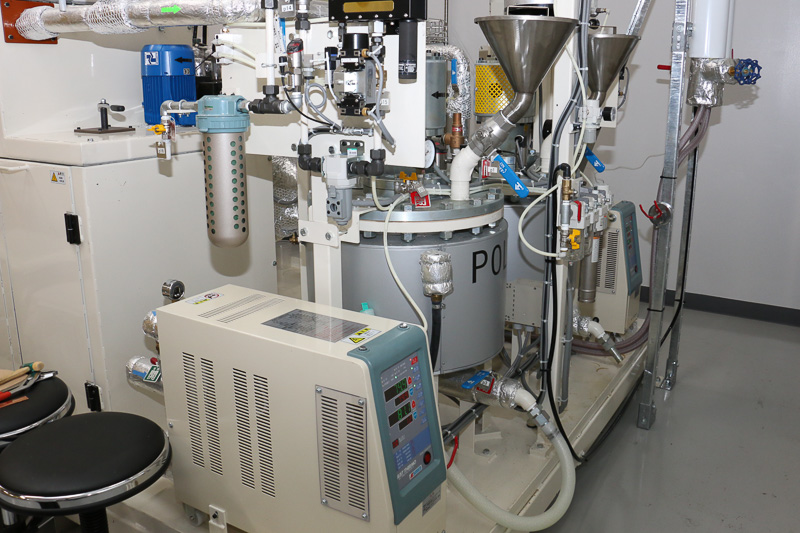 大型成形機の右手奥に、材料のポリウレタンやエポキシを供給するタンクを配置