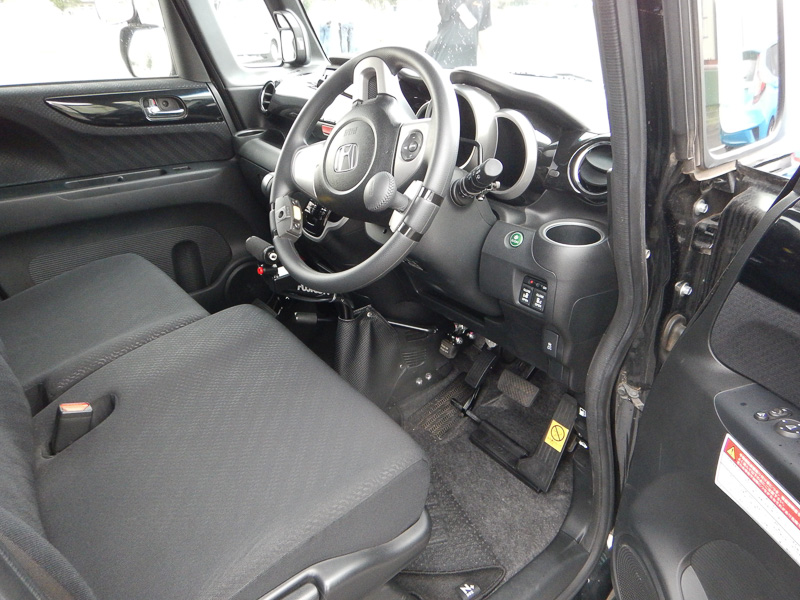 足下のブレーキと足踏み式パーキングのあいだに左足用アクセルペダルを追加。ステアリングには「ハンドル旋回ノブ」が装着されている