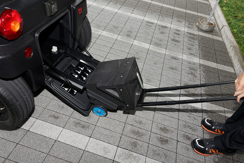 着脱式バッテリーは車体後部から取り外せる。かなりの重量だが旅行用のキャリーバッグのようにタイヤと伸縮ハンドルが付いているため、女性でも容易に移動できるという。充電器と一緒に宅内に運び入れて充電できる