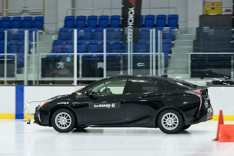 アイスガード 5プラス（白いプリウス）と、アイスガード 6（黒いプリウス）の制動距離の違い。20km/hからのブレーキで、壁の青いペイントからアイスガード 6の制動距離が短いことが分かる