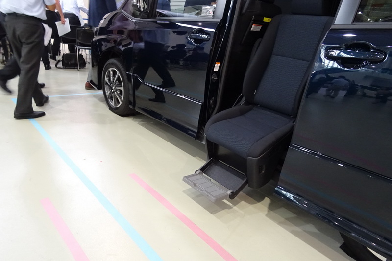 ピンクのラインがドアから50cm、ブルーのラインが100cm。従来のもの（左）に比べ、サイドリフトアップチルトシート車（右）は車体からシートが張り出す量が半分以下に