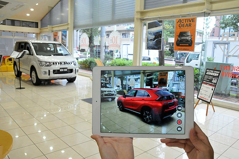 シートに専用のアプリを立ち上げたiPadをかざすとエクリプス クロスが現われる。目黒店ではエクリプス クロスとの比較のために「デリカD：5」を展示。デリカD：5のボディサイズは4730×1795×1870mm（全長×全幅×全高）だが、エクリプス クロスを実寸大で並べてみるとエクリプス クロスの方が少し大きく感じた