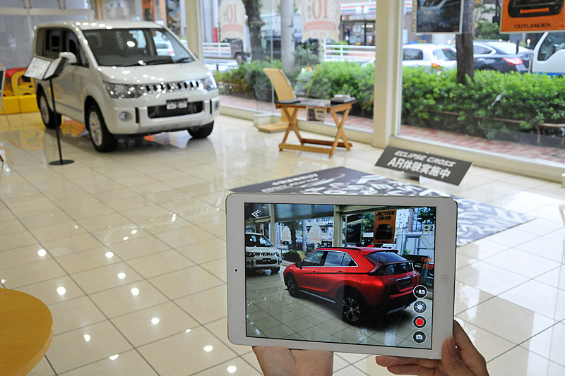 シートに専用のアプリを立ち上げたiPadをかざすとエクリプス クロスが現われる。目黒店ではエクリプス クロスとの比較のために「デリカD：5」を展示。デリカD：5のボディサイズは4730×1795×1870mm（全長×全幅×全高）だが、エクリプス クロスを実寸大で並べてみるとエクリプス クロスの方が少し大きく感じた