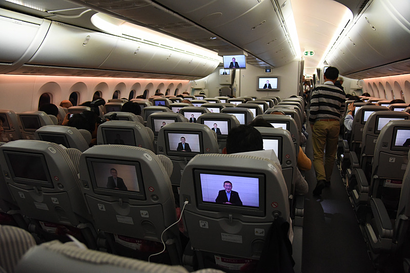 吉永社長の機内ビデオ挨拶が始まった。こちらはエコノミークラス。チャーター便ならではのプログラム