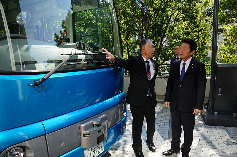 先進モビリティ株式会社 代表取締役社長 青木啓二氏（左）が松山政司内閣府特命担当大臣（右）に今回の実証実験に利用する車両を説明