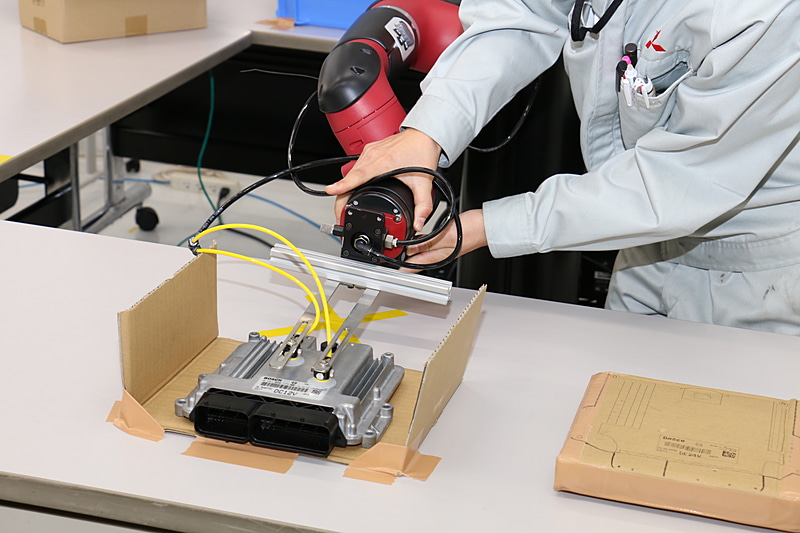 1回置いたECUを再度持ち上げるとき、アームのケーブルが段ボールに引っかかって動作がストップ。そこで担当者がアームを動かし、回避する動き方をSawyerに学習させた。アームを動かすことで動作を教える「ダイレクトティーチング」という機能を持ち、プログラミング知識がない人でも動作を教えることができるようになっている