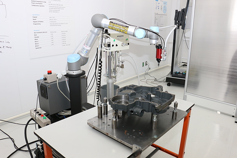 エンジンのシール材塗布を自動化する試み。ここでは動作確認のため、アームの先を水で濡らして隔壁部分の上をなぞっていた