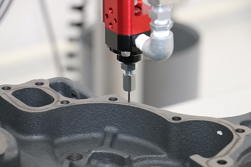 エンジンのシール材塗布を自動化する試み。ここでは動作確認のため、アームの先を水で濡らして隔壁部分の上をなぞっていた