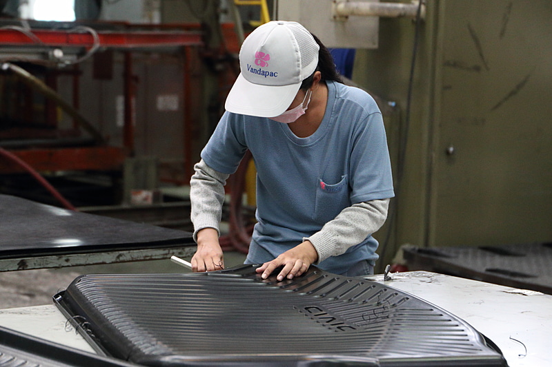 真空成型されたトランクトレイの余分な“耳”を人の手でカット