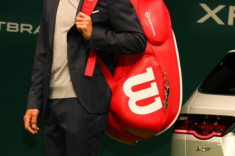 ラケットバッグを背負ってジャガーブランドチャームを紹介。ジャガーのブランドロゴが滑らかな金属で立体化されている