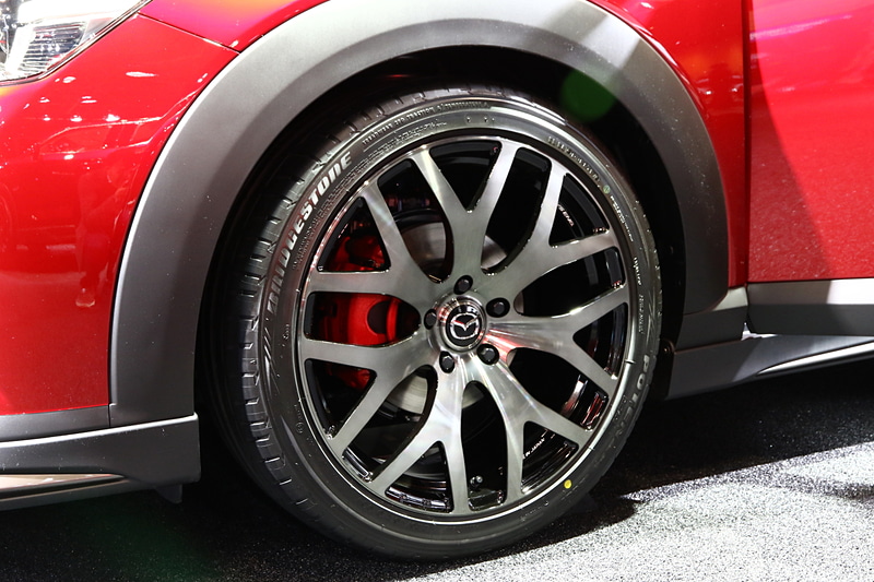 ディーラーオプションとなるMAZDASPEEDのエクステリアパーツを装備したCX-3。マフラーはMAZDASPEEDの特別仕様で、参考出品となる。足まわりやブレーキもカスタマイズパーツを装着していて、ブレーキは赤の塗装を施したペイントキャリパー、ホイールはRAYS製の「WALTZ S7」、タイヤはブリヂストン「POTENZA S001」。サスペンションは、MAZDASPEEDの車高調整式で、フロント30mm、リア25mmを下げている。ブレーキとタイヤ・ホイール、サスペンションともに参考出品となる