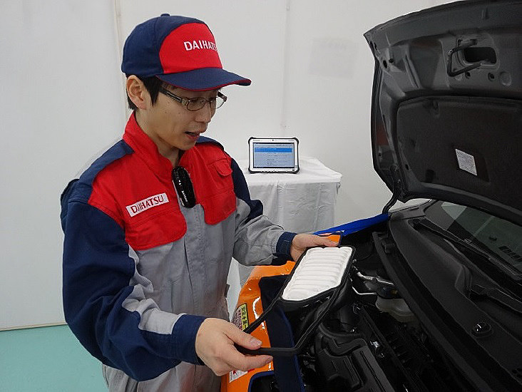 エアクリーナエレメントを点検する様子。胸元のウェアラブルマイクを通し、奥のタブレット端末に点検結果が入力される