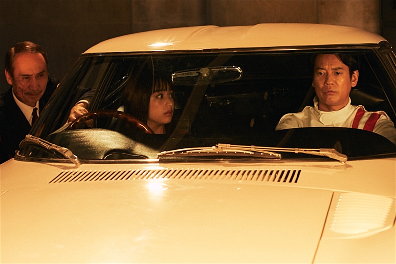 唐沢寿明さん（右）演じる白いレーシングスーツの男が白雪の前に現れる