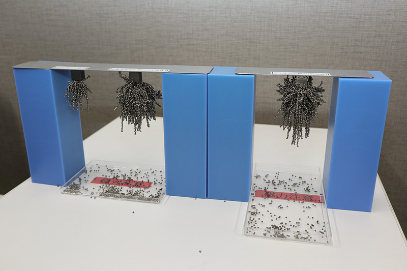 説明会で展示された磁力を比較する技術サンプル。左がフェライト磁石、中央が既存のネオジム磁石、右が省ネオジム耐熱磁石。細かな金属製の粒を使い、中央と右の磁石で大きな差がないとアピールした