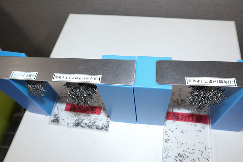 説明会で展示された磁力を比較する技術サンプル。左がフェライト磁石、中央が既存のネオジム磁石、右が省ネオジム耐熱磁石。細かな金属製の粒を使い、中央と右の磁石で大きな差がないとアピールした