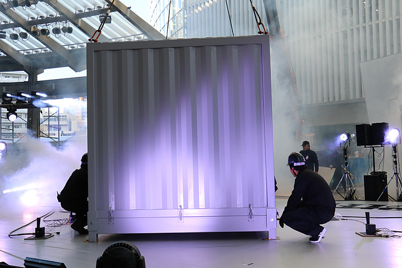 クレーンを使ってステージ上に移動されたコンテナ内からニューマシンが登場