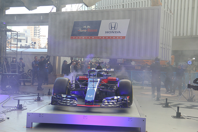 クレーンを使ってステージ上に移動されたコンテナ内からニューマシンが登場