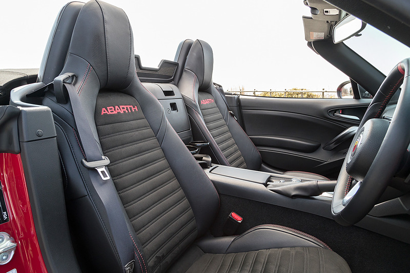 ブラックを基調に各所にレッドステッチなど赤色の加飾が与えられたアバルト 124 スパイダーのインテリア。アルミニウム製のペダル類、垂直に近いステアリングホイール、短いシフトレバーなどがスポーティなキャラクターを強調している