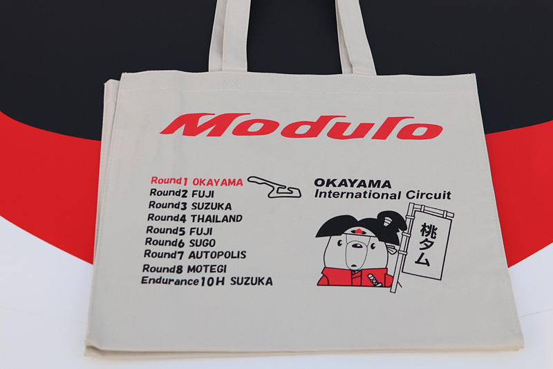 SUPER GTの各会場でホンダアクセスが配布しているオリジナルグッズ。岡山では“桃タム”をあしらった「“桃タム”トートバッグ」が用意された。このトートバッグに「道上選手＆大津選手」「Moduloスマイル＆Moduloプリティ」にサインしていただき、Car Watch読者各1人、計2人にプレゼント