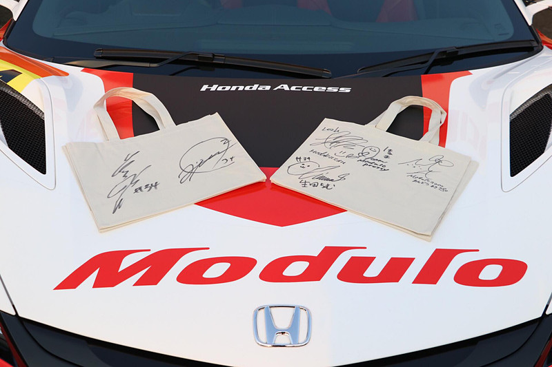 SUPER GTの各会場でホンダアクセスが配布しているオリジナルグッズ。岡山では“桃タム”をあしらった「“桃タム”トートバッグ」が用意された。このトートバッグに「道上選手＆大津選手」「Moduloスマイル＆Moduloプリティ」にサインしていただき、Car Watch読者各1人、計2人にプレゼント