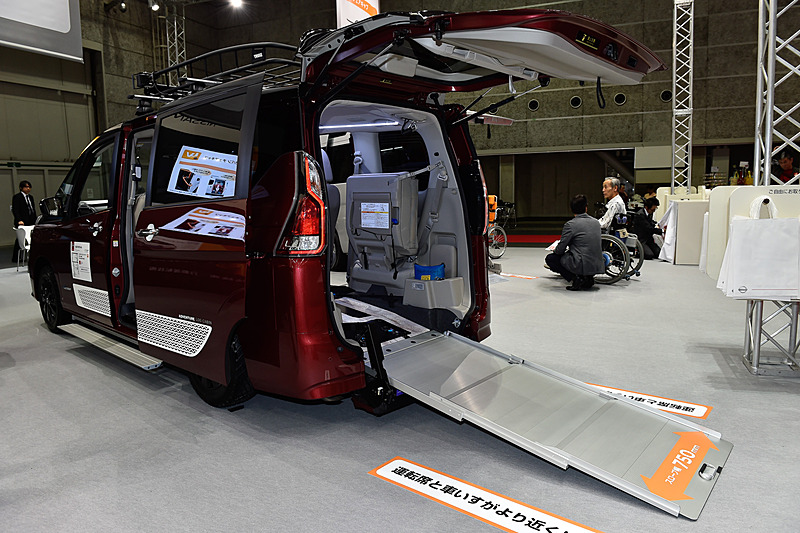 セレナ チェアキャブ スロープタイプ 車いす2名仕様。展示用にラッピングシートで車両の上側をブラックアウト。フロントバンパーやドアパネルにはホワイトのステッカーを設置したほか、オフロード用タイヤを装着して力強さをアピールする