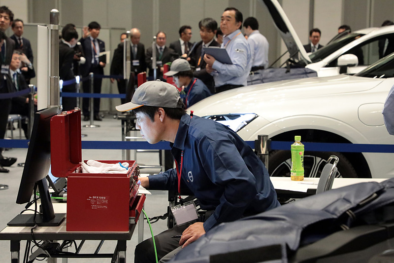 技能試験中の光景。かなり難しい問題設定だったようで、テクニシャンといえども苦戦している方が多かった。なお、いまどきはアレコレ外してチェックするのではなく、診断機をフル活用するので修理といっても診断中はPCを見る時間のほうが長い