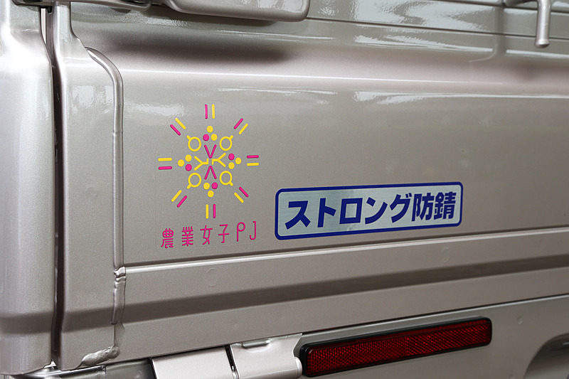 荷台を錆に強くするオプションの荷台フルメッキ/厚メッキ加工の「ストロング防錆パック」と、「農業女子パック」が装備されていることを示すステッカー