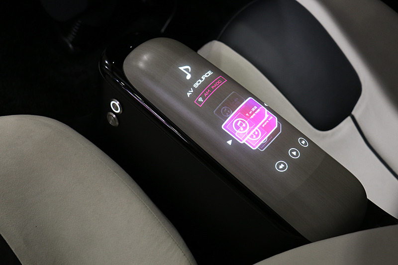 デラグラスでは樹脂表面に焦点を結ばせることが可能になり、内側から投射した映像をディスプレイのように表示できる。展示では木目調パネルのアームレストにエアコンやオーディオの情報が次々に表示されていた