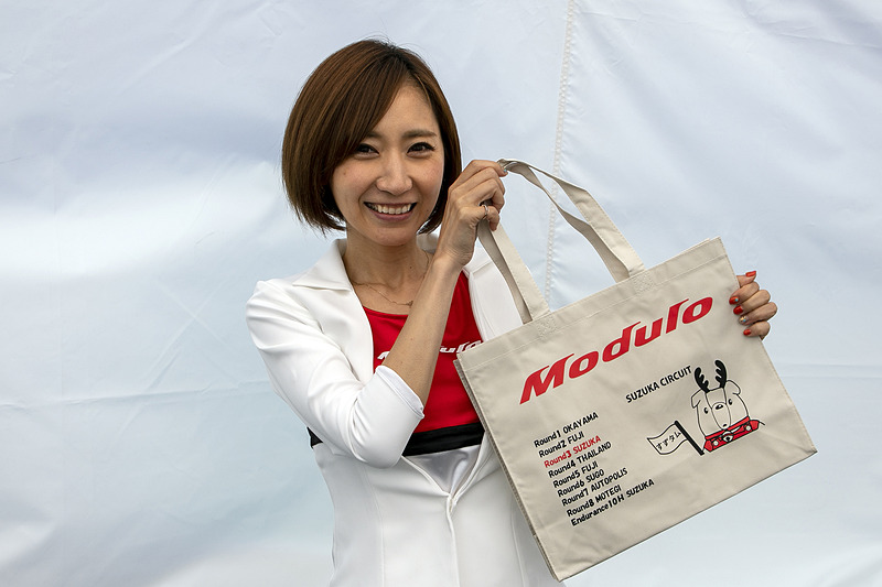 物販コーナー。ホンダアクセスのマスコットキャラ「くるタム」のぬいぐるみを購入した人には、サーキットごとの「ご当地くるタム」が描かれた特製トートバッグを数量限定でプレゼント。Moduloスマイルの水村リアさんが持つ鈴鹿仕様のトートバッグには、鹿の角を付けた「すずタム」が描かれている