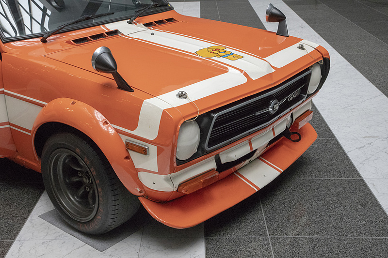 バンパーとグリルまわりの加飾パーツが取り去られている。ライトも外されていてカバーが付く。大型のスポイラーも装着。下を覗くと裏面に飛び石などから防御するためのゴムが貼ってあった