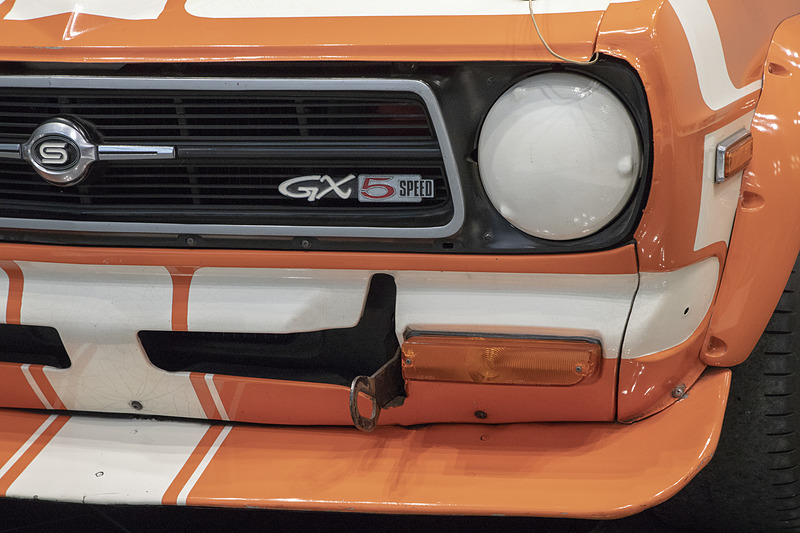 バンパーとグリルまわりの加飾パーツが取り去られている。ライトも外されていてカバーが付く。大型のスポイラーも装着。下を覗くと裏面に飛び石などから防御するためのゴムが貼ってあった