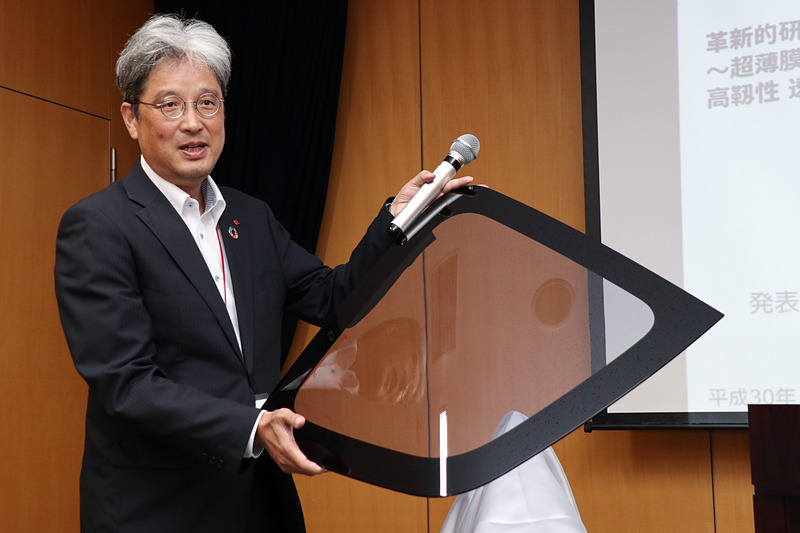 住友化学が開発した「PMMAをベースとした軽くて頑丈な透明樹脂」を使ったリアウィンドウのデモ製品。持っているのは住友化学株式会社 石油化学品研究所 所長の永松龍弘氏