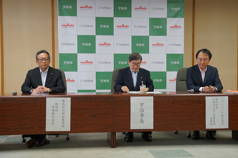 「Iotを活用して路面情報を検知する実証実験に関する説明会」に出席した、村田製作所 取締役常務執行役員 岩坪浩氏（左）、宇治市市長の山本正氏（中央）、ソフトバンク 執行役員 広域法人第二営業本部 本部長 清水繁宏氏（右）