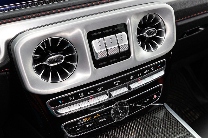 左右のエアアウトレットに特徴的な円形ヘッドライトの形状を採用するとともに、ウインカーをイメージしたスピーカーなどを装着。助手席前方のグラブハンドルや、3つのディファレンシャルロックを操作するクローム仕上げのスイッチなどは新型でも継承する一方で、厳選されたレザーや上質なウッドトリム、随所に施されたシルバー加飾などを用いることでラグジュアリーさも強調