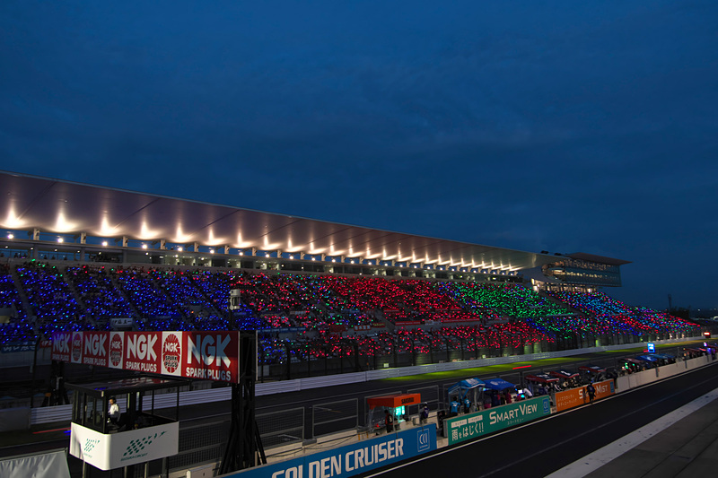 日没後、グランドスタンドの観戦者が各メーカーチームカラーのライトを振って応援